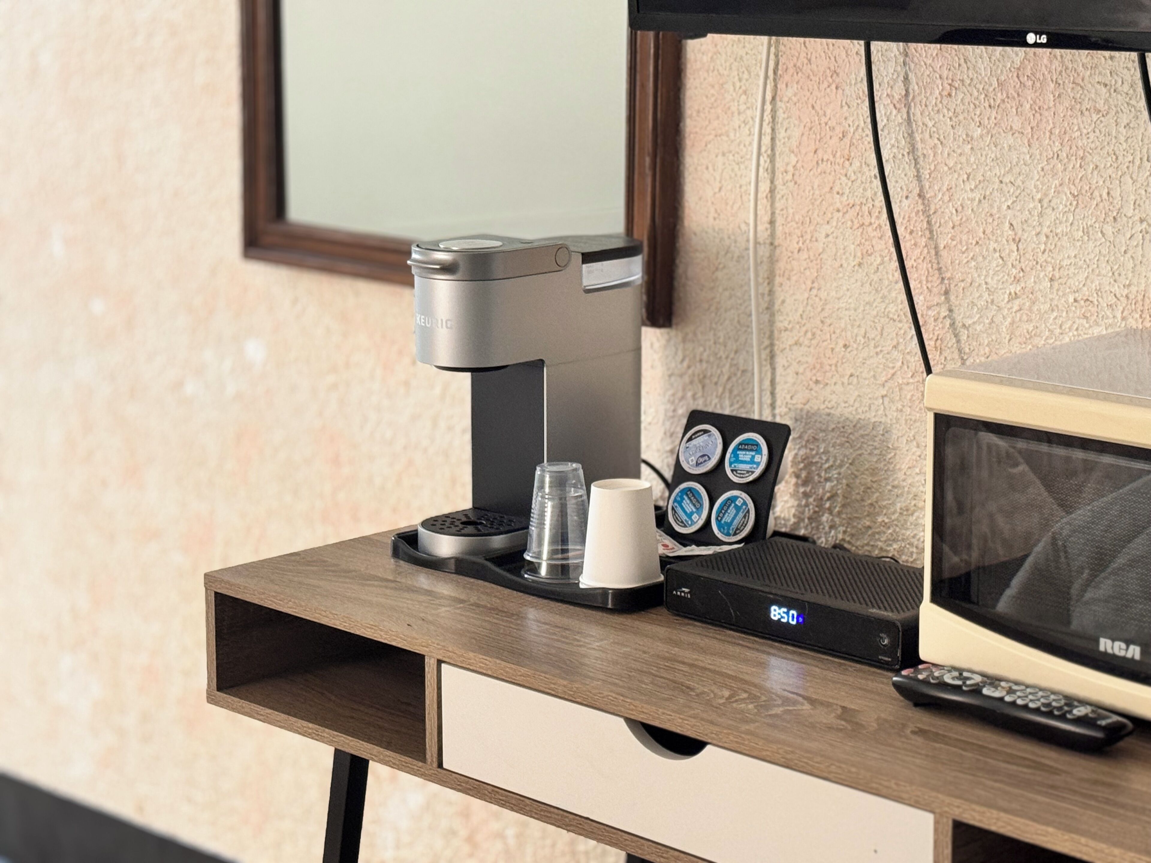 Una máquina de café, un control remoto y un reloj digital sobre un escritorio de madera.