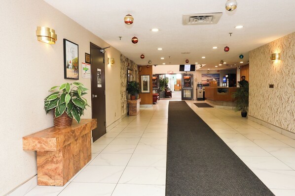 A hotel lobby with a reception desk, potted plants, a black carpet, and a wall with framed pictures.