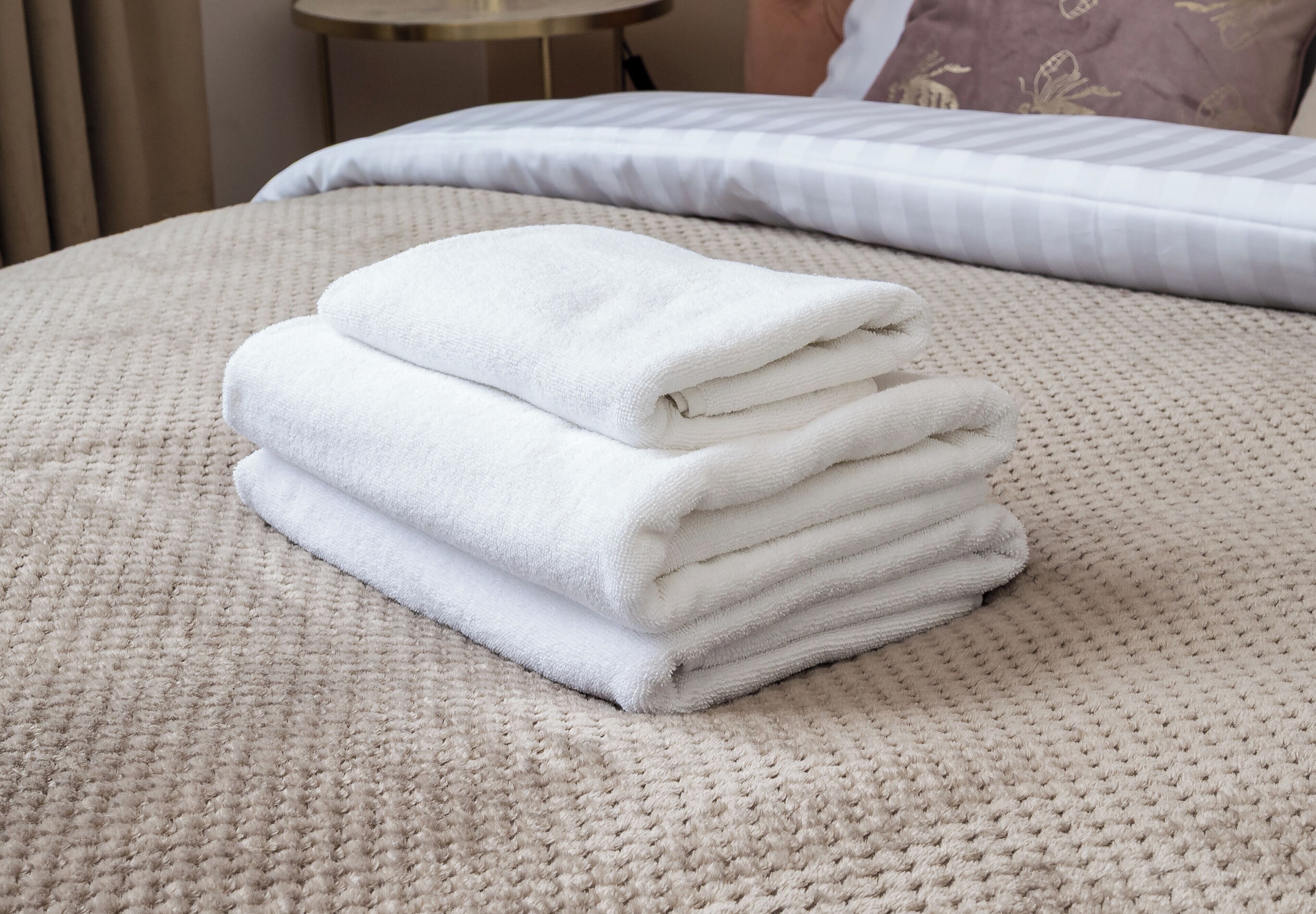 En pænt foldet stak hvide håndklæder på en meleret beige dyne.