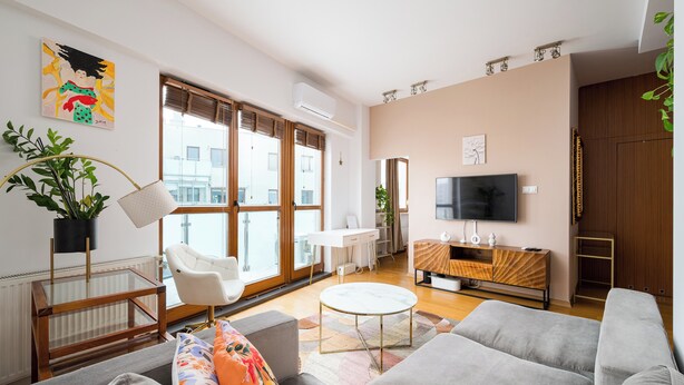 A modern living room with a grey sofa, a white armchair, a glass coffee table, and a TV on the wall.