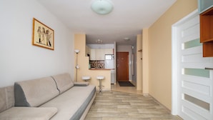 A modern living room with a sofa, a kitchen in the background, and a hallway leading to a door. - Solec Powiśle Harmony Apartment (Warszawa)