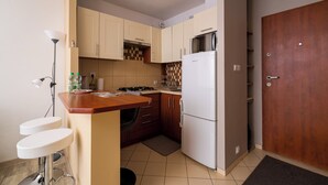 A compact kitchen with a refrigerator, stove, and sink. There is a wooden door and a small bar stool. - Solec Powiśle Harmony Apartment (Warszawa)