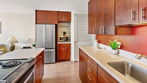 Eine moderne Küche mit Holzschränken, einem Edelstahlkühlschrank, einer Mikrowelle und einem Spülbecken.