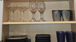 Ett köksskåp med hyllor som innehåller olika typer av köksredskap, inklusive skålar, tallrikar, en stekpanna, vinglas och koppar.