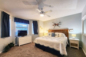 A bedroom with a bed, a ceiling fan, a TV, and a window with curtains.