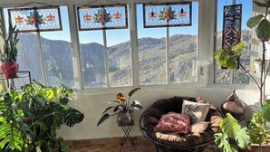 Et solfyldt rum med store vinduer, et hyggeligt opholdsområde og flere potteplanter.