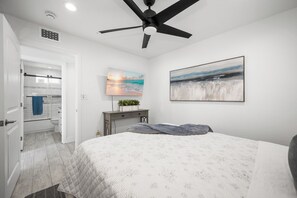 A bedroom with a bed, a ceiling fan, a painting, and a bathroom visible through an open door. - Patio on the Boardwalk steps to the Ocean (Newport Beach)