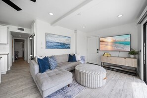 Ein modernes Wohnzimmer mit einem grauen Ecksofa, einem gestreiften Ottomanen und einem großen Flachbildfernseher auf einer Holzkonsole.