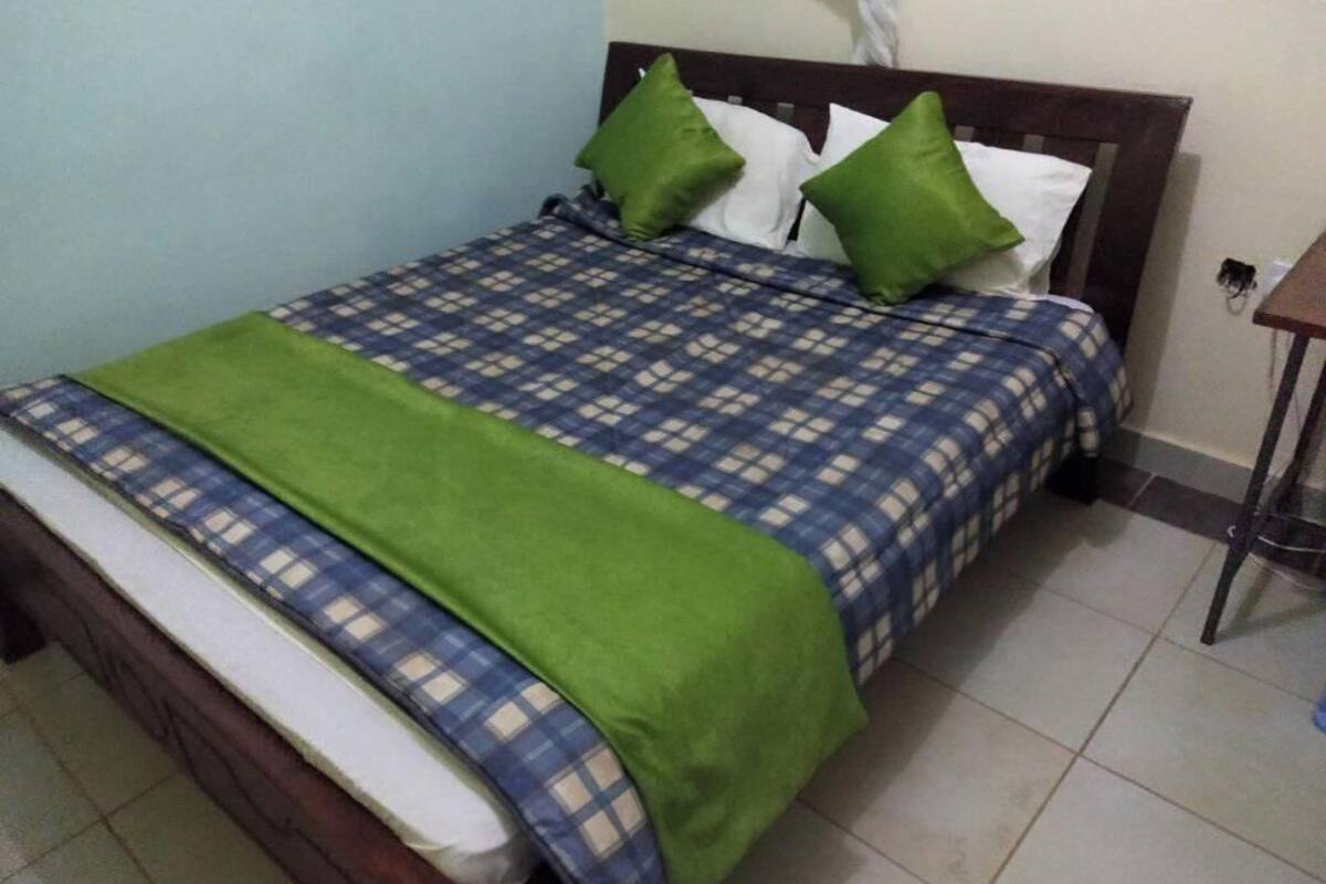 Ein Bett mit kariertem Bettbezug, grünen Kissen und einer grünen Tagesdecke.