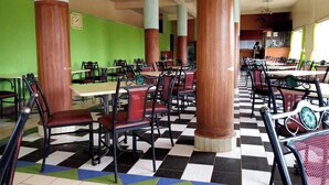 Un espace repas avec un sol à carreaux, plusieurs tables et chaises, et des murs verts.