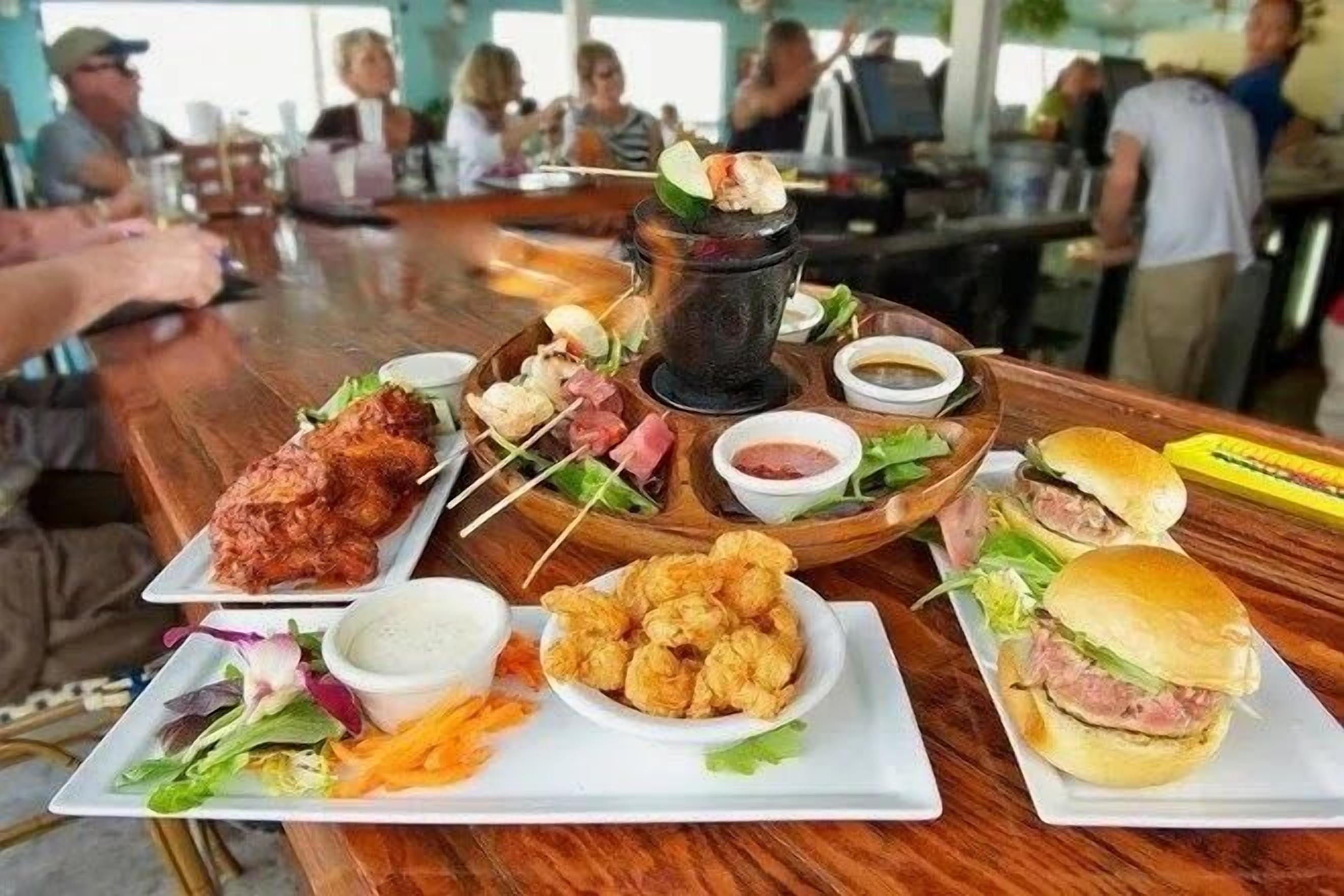 A dining table with various dishes including fried items, a burger, and a skewer with meat.