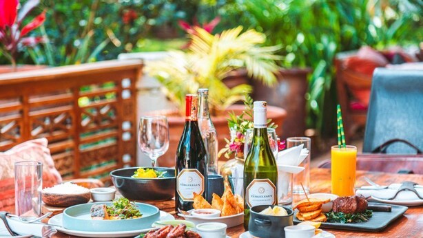 Une table à manger dressée avec différents plats, des bouteilles de vin et un verre de jus d’orange.