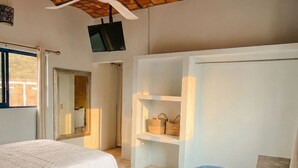 A bedroom with a bed, a TV mounted on the wall, a wardrobe, and a shelf with bags. - Casitas Aramara | Sunset Loft in Lo de Marcos (Lo de Marcos)