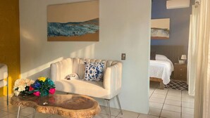 A hotel room with a sofa, a wooden coffee table with flowers, and a painting on the wall. - Casitas Aramara | Sunset Loft in Lo de Marcos (Lo de Marcos)