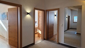 Un couloir avec des portes en bois et des luminaires, qui mène à une chambre dotée d’une fenêtre.