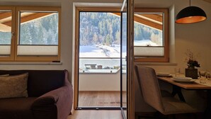 Une pièce chaleureuse avec un plafond en bois, une table à manger dressée pour deux personnes et une vue sur un paysage enneigé par de grandes fenêtres.