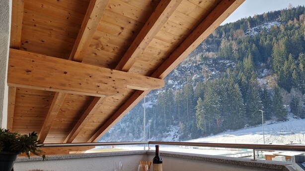 Un balcon en bois avec une table dressée pour deux personnes, offrant une vue sur un paysage montagneux enneigé.