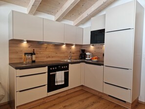 Eine moderne Küche mit Holzbalken, weißen Schränken, einem eingebauten Ofen und einer Kaffeemaschine.