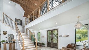 A spacious interior with a wooden staircase, a large window with a view, and a cozy seating area. - Luxe Eagles Nest Home: 3-Tier Deck, Hot Tub, Fire Pit & Sunset Views! (Banner Elk)