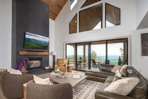 Ein modernes Wohnzimmer mit Kamin, Ledersofa und einem großen Fenster mit Blick auf eine reizvolle Landschaft.