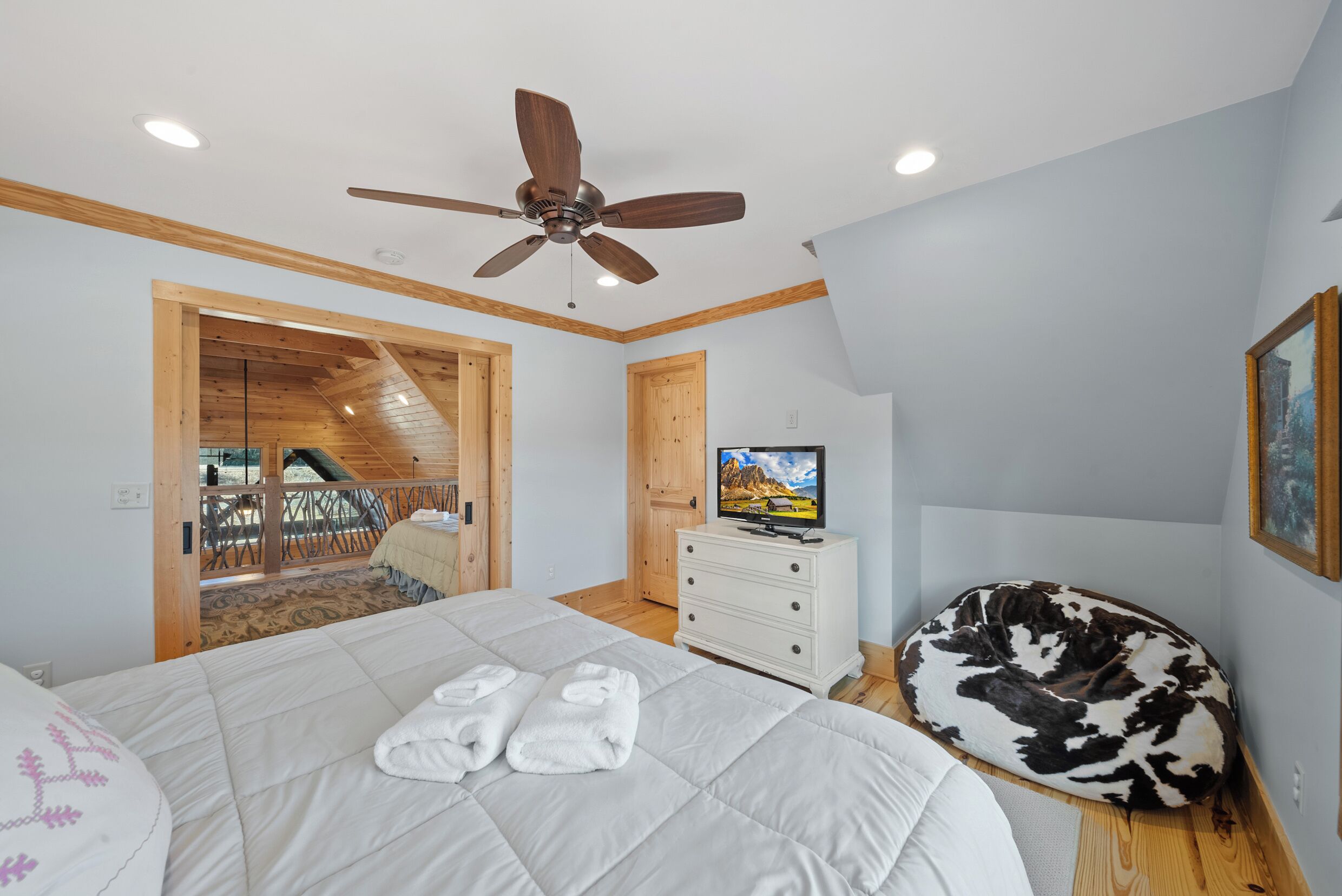 A bedroom with a bed, a ceiling fan, a television, and a wooden door leading to a balcony.