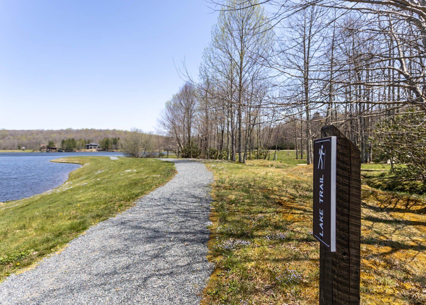 A gravel path beside a lake with a sign indicating a trail.