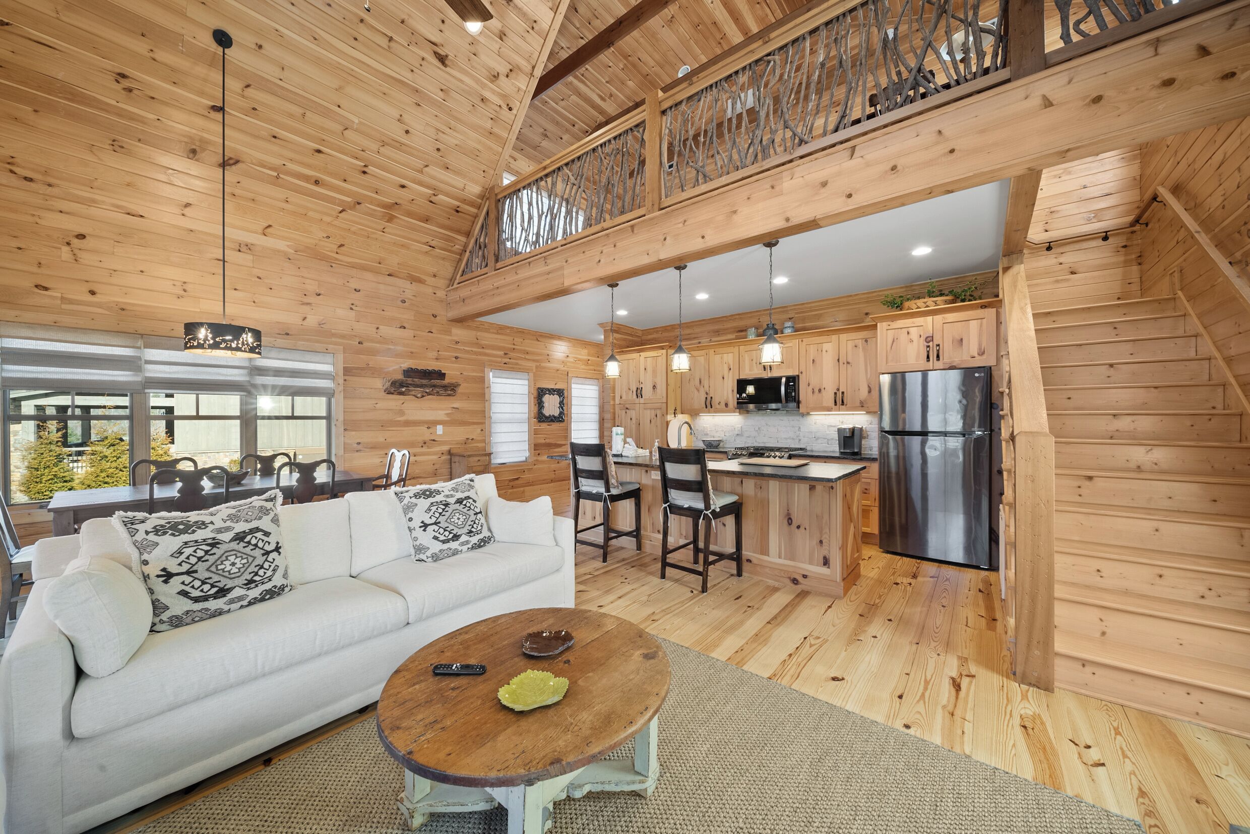 A spacious wooden cabin with a dining area, kitchen, and a white sofa with patterned cushions.