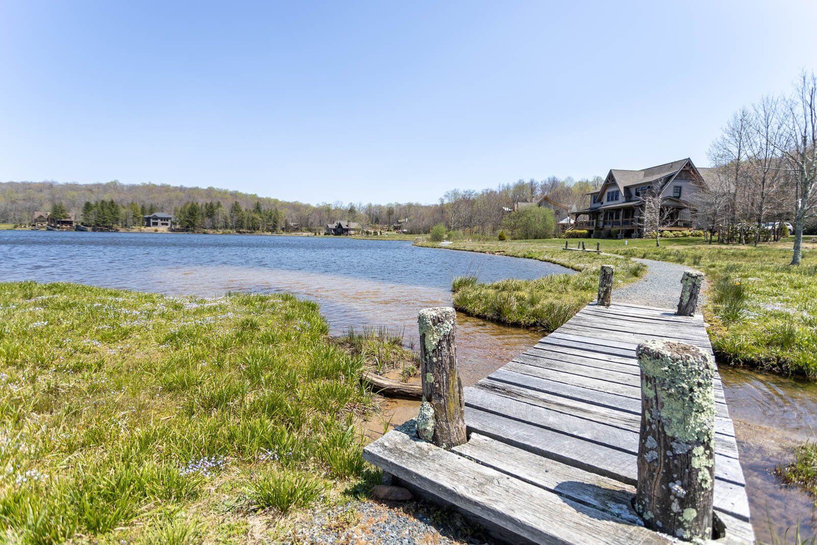 A wooden dock leading to a house by a lake with a clear sky.