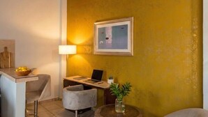 A compact living space with a desk, a chair, a laptop, a lamp, a bowl of fruit, and a framed picture on the wall. - Casitas Aramara | Coastal Studio in Lo de Marcos (Lo de Marcos)