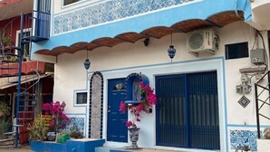 A two-story building with a blue and white facade, a central door with a decorative arch, and a balcony with a blue railing. - Casitas Aramara | Coastal Studio in Lo de Marcos (Lo de Marcos)