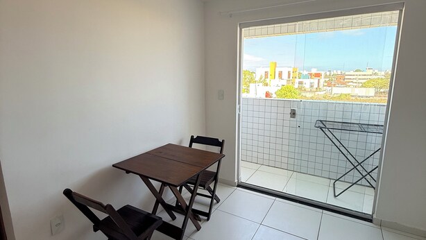 A small balcony with a table and chairs, a view of buildings, and a tiled floor. - Comfortable and well-located apartment (João Pessoa)
