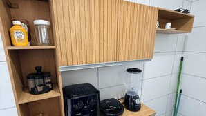 A kitchen with wooden cabinets, a coffee maker, a blender, and a mop. - Comfortable and well-located apartment (João Pessoa)