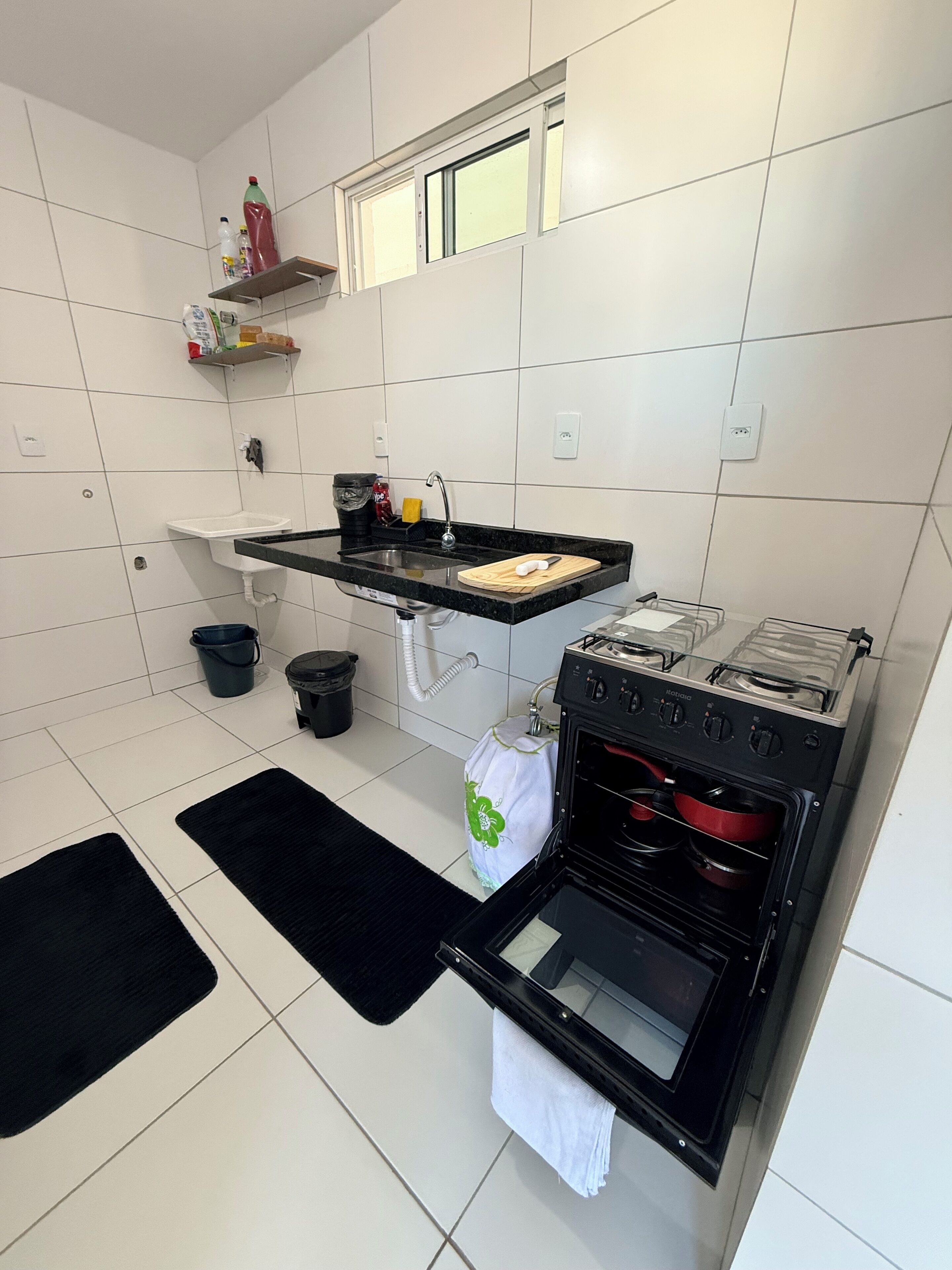 A kitchen with a black countertop, a sink, a stove, and a window above the sink.