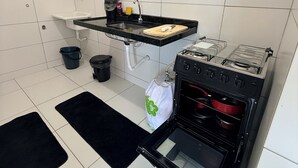 A kitchen with a black countertop, a sink, a stove, and a window above the sink. - Comfortable and well-located apartment (João Pessoa)