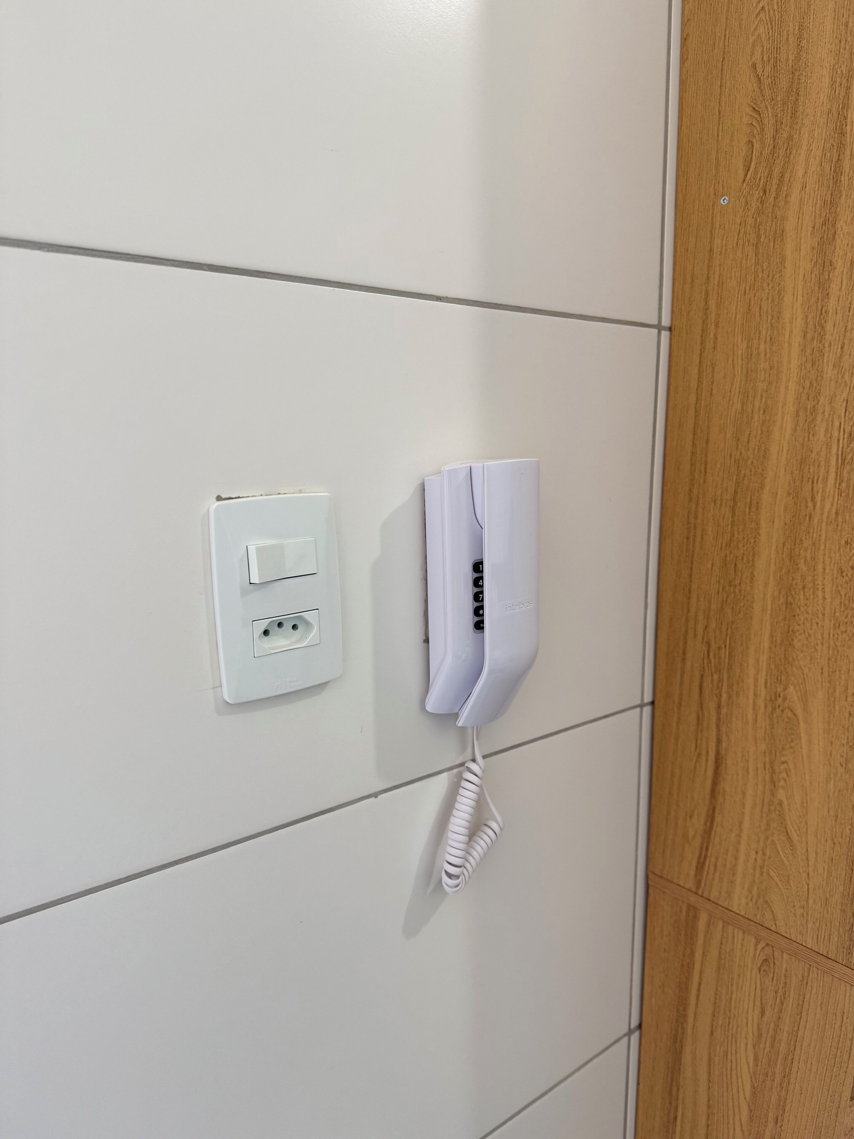 A white telephone mounted on a wall with a wooden panel to the right.
