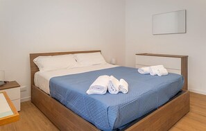 A neatly made bed with a blue bedspread and white pillows, a wooden headboard, and a folded towel on the footboard. - Lovely home in Santa Croce Camerina with house sea view (Santa Croce Camerina)