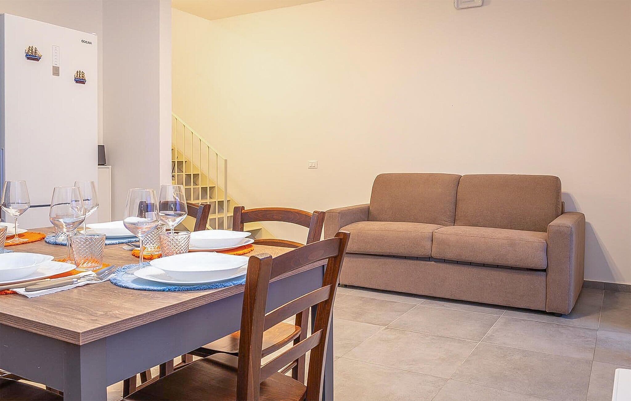 Un comedor con una mesa de madera dispuesta para cuatro, sillas y un sofá al fondo.