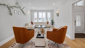 Un salon moderne avec un canapé blanc, deux fauteuils orange, une table basse en verre et une branche décorative accrochée au mur.