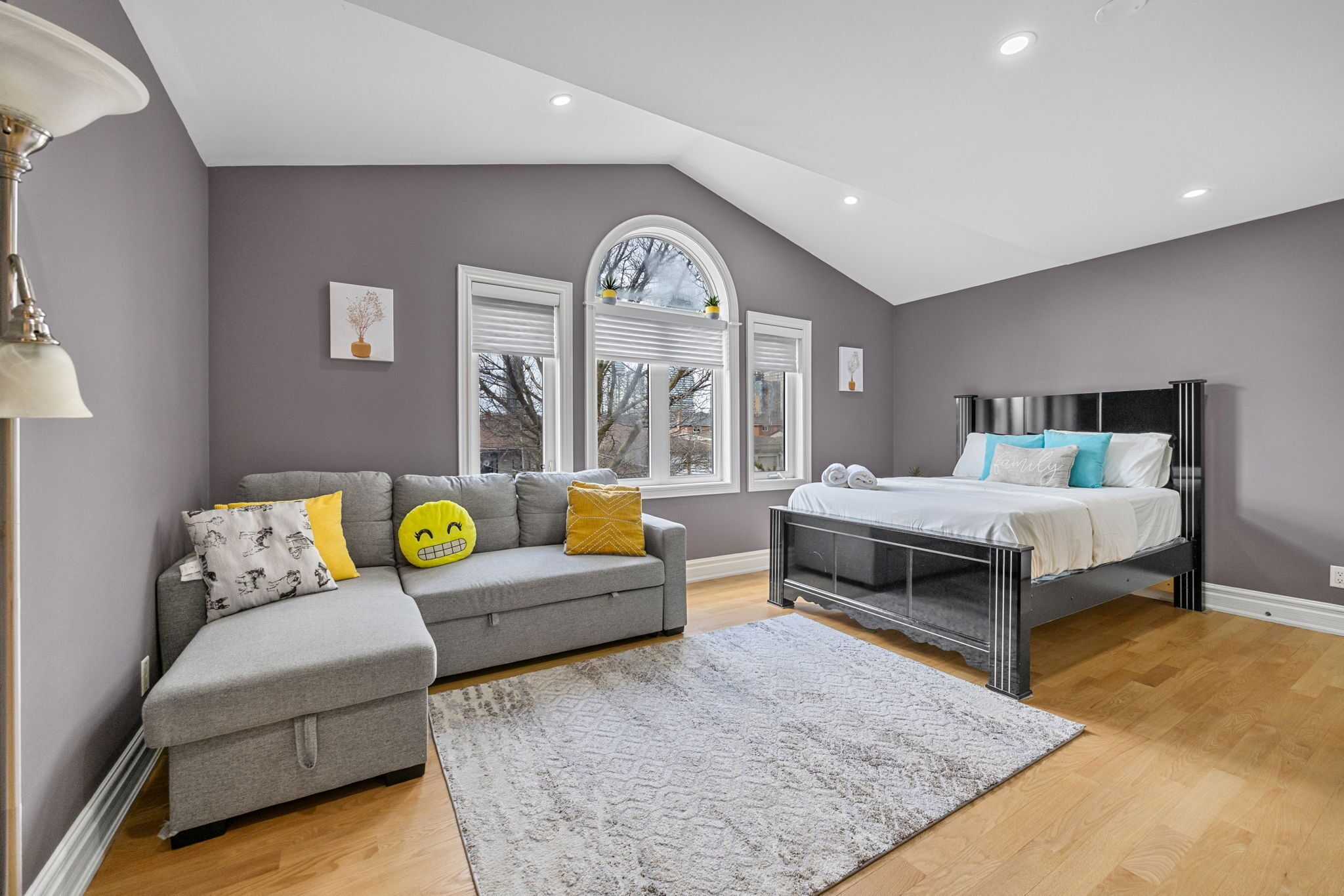 A bedroom with a bed, a grey sofa, and a window with white shutters.