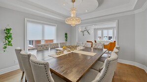 Une salle à manger spacieuse, avec une grande table en bois, des chaises rembourrées et un lustre.