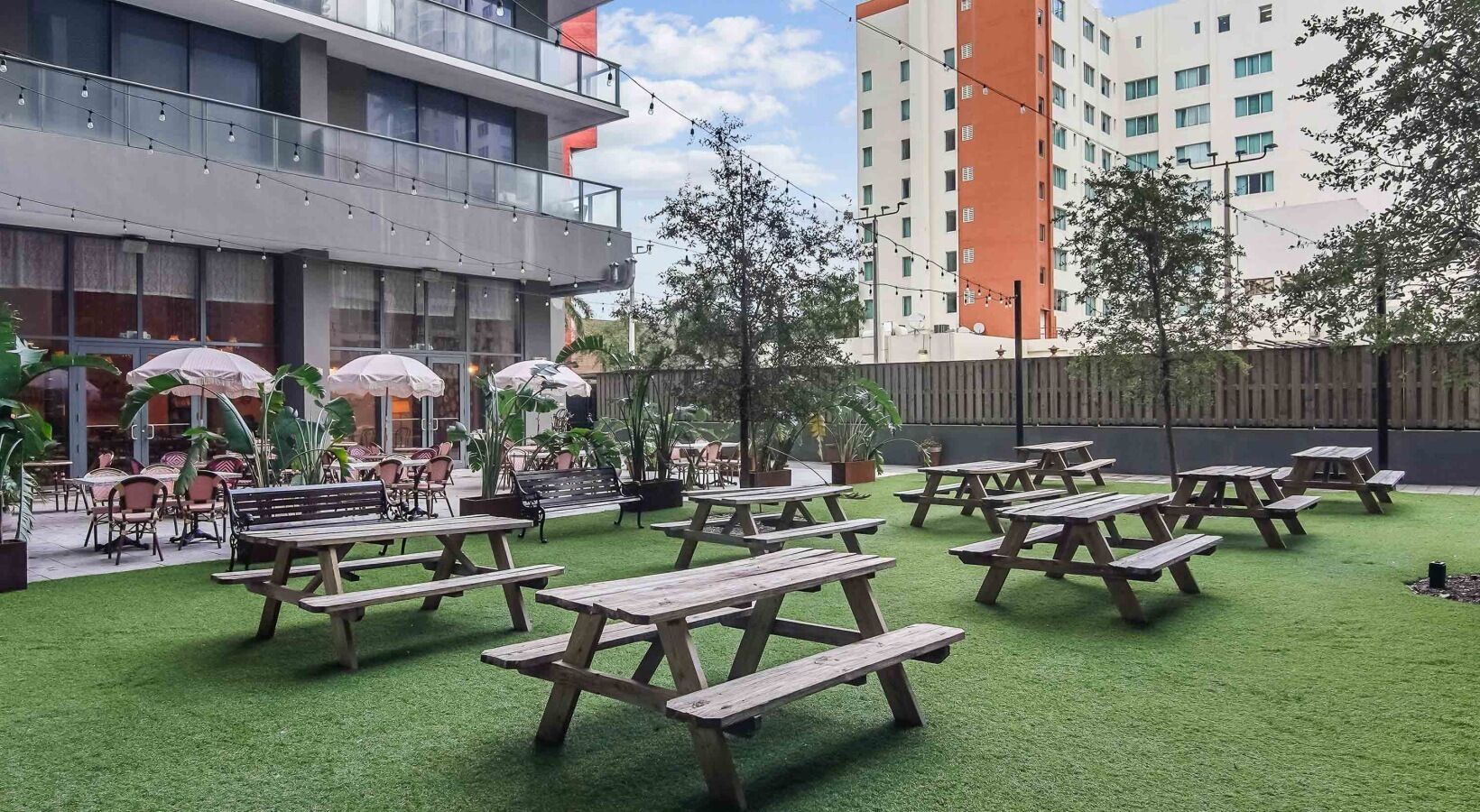 An outdoor patio area with wooden picnic tables and chairs, surrounded by artificial grass.