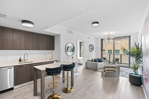 A modern kitchen with a central island, bar stools, and a dining table. There is a balcony with a view of buildings and a potted plant. - Private 2bed/2bath, Sun-Filled Modern Condo in the Heart of Downtown Miami (Miami)