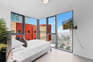 A modern bedroom with a large bed, a TV mounted on the wall, and a city view through large windows. - Private 2bed/2bath, Sun-Filled Modern Condo in the Heart of Downtown Miami (Miami)