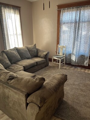 Sala de estar com um sofá cinzento, uma cadeira branca e cortinas estampadas.