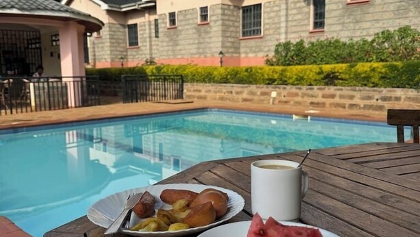 A poolside table with plates of food and a coffee cup, surrounded by a pool and a building with stone walls and windows. - Alem Resort Tawa (Tawa)