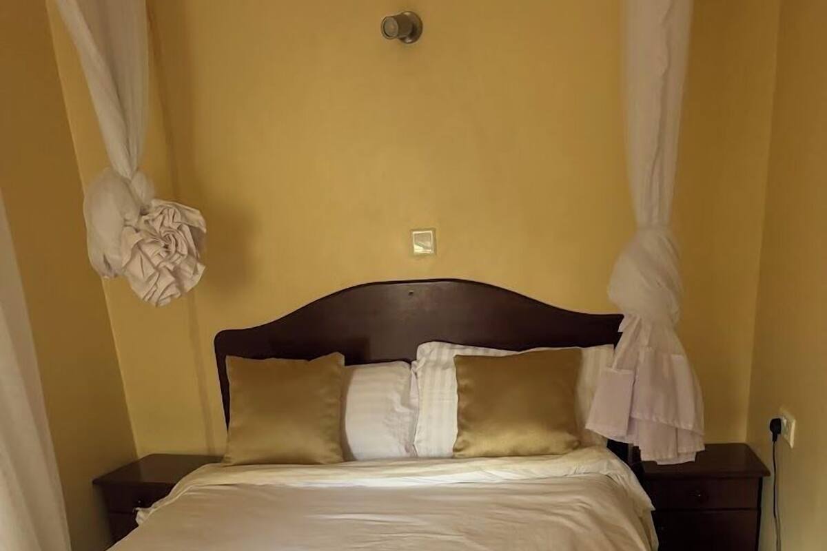 A neatly made bed with white and beige bedding, a wooden headboard, and a bedside table with a lamp.
