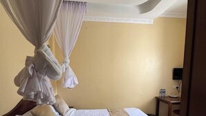 A hotel room with a bed, a nightstand, a small table with a chair, and a television on the wall. - Alem Resort Tawa (Tawa)
