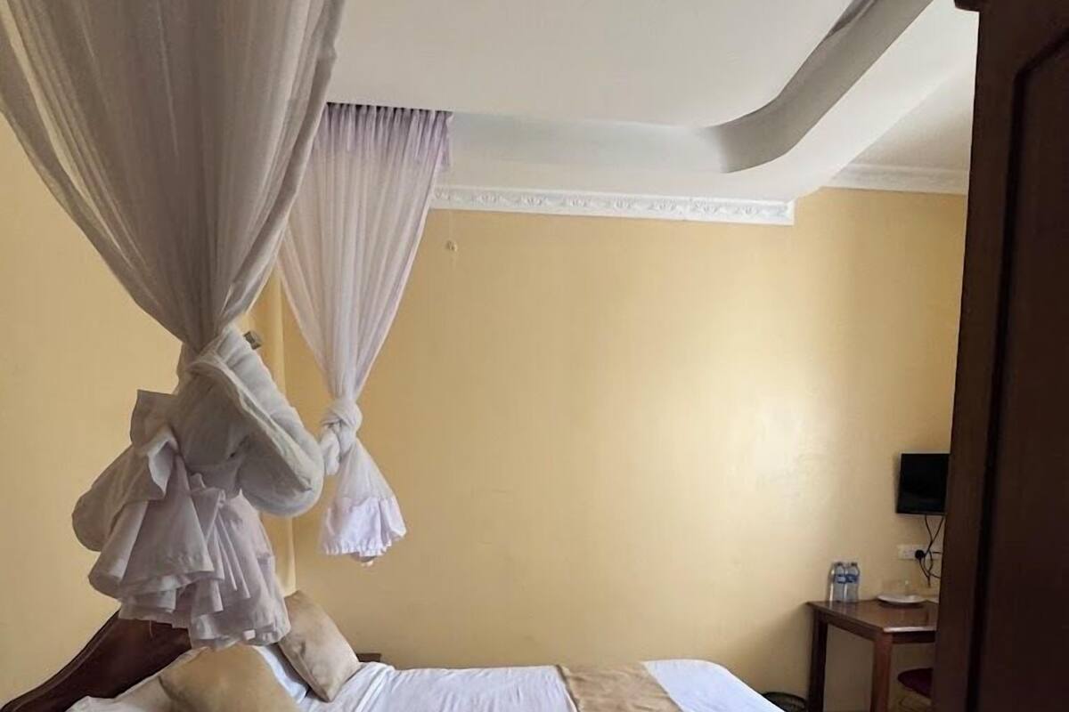 A hotel room with a bed, a nightstand, a small table with a chair, and a television on the wall.