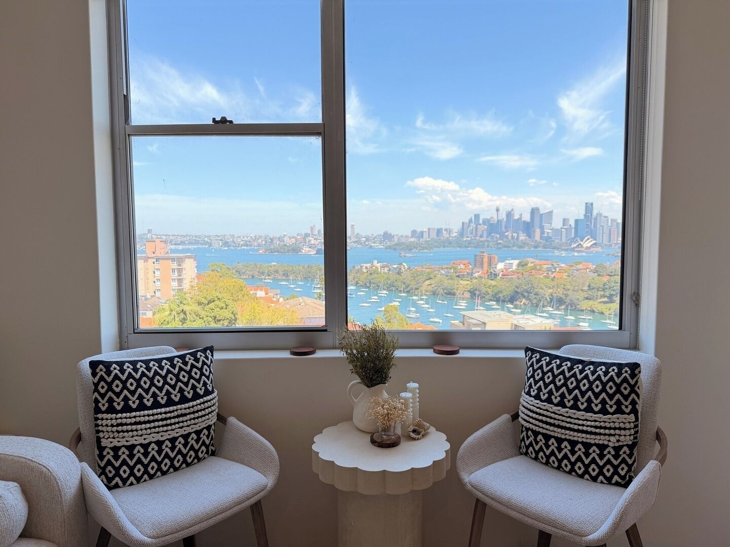 A room with two chairs facing a large window overlooking a cityscape and water.