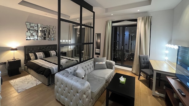 Ein modernes Wohnzimmer mit einem großen Bett, einem grauen Sofa, einem schwarzen Couchtisch und einem Fernseher.